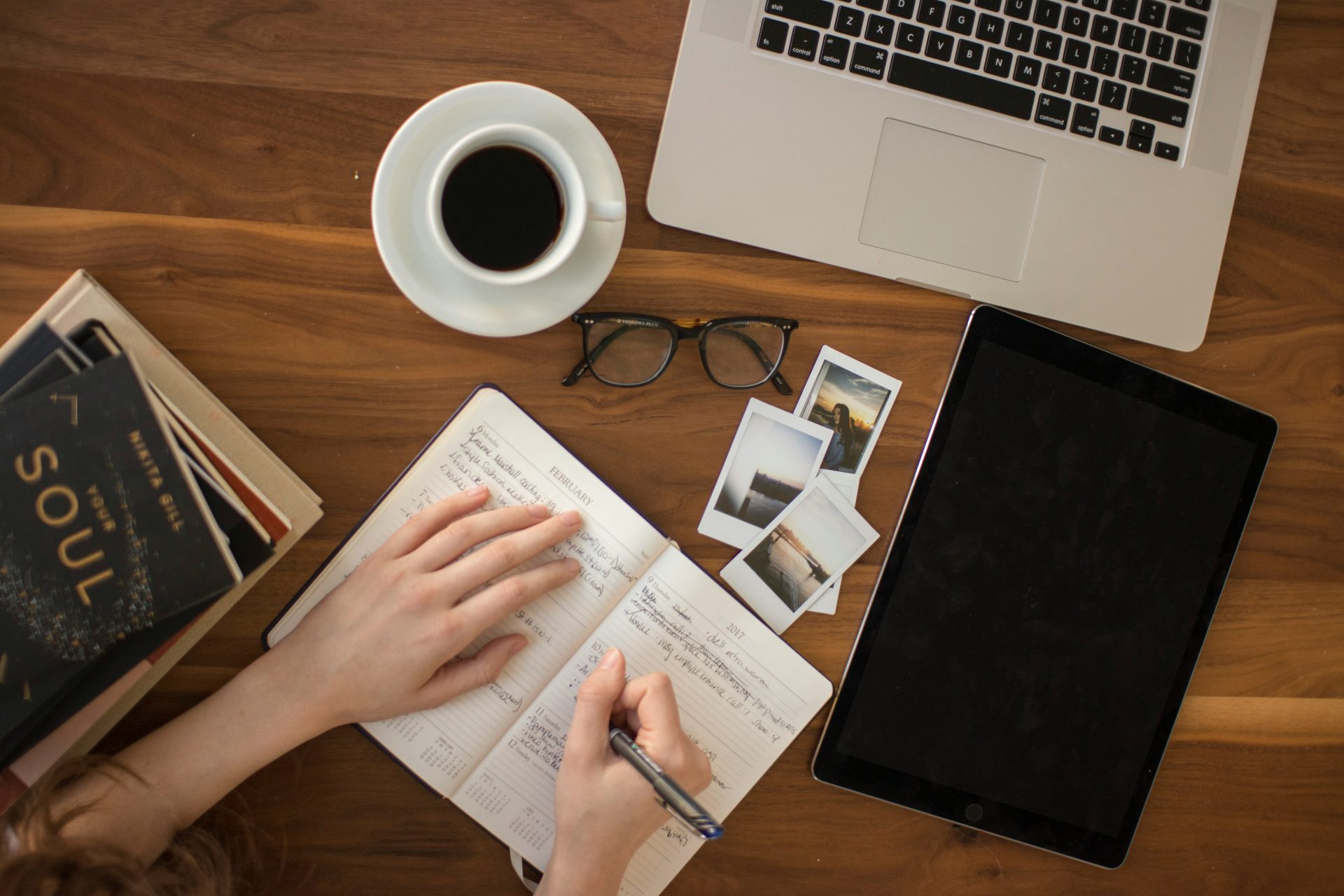 Persona escribiendo en una libreta con café y un portátil al lado